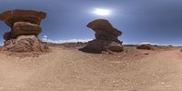 a panorama camera shot of two rock formations in a desert area, with a bright sun setting over the rocks