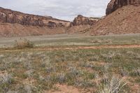 two horses grazing in a desert near rocks and grass and a hill of dirt with mountains in the background