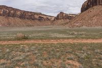 two horses grazing in a desert near rocks and grass and a hill of dirt with mountains in the background