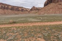 two horses grazing in a desert near rocks and grass and a hill of dirt with mountains in the background