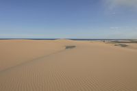 a person walking in the desert on the beach with an umbrella over their head and a blue ocean in the distance