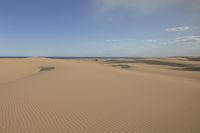 a person walking in the desert on the beach with an umbrella over their head and a blue ocean in the distance