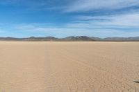 a desert with the desert ground covered in sand and a lone person walking across it