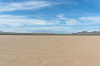 a desert with the desert ground covered in sand and a lone person walking across it