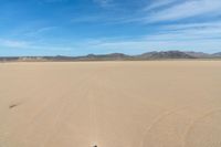 a desert with the desert ground covered in sand and a lone person walking across it