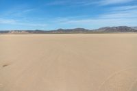 a desert with the desert ground covered in sand and a lone person walking across it