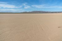 a desert with the desert ground covered in sand and a lone person walking across it