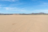 a desert with the desert ground covered in sand and a lone person walking across it