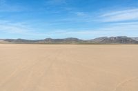 a desert with the desert ground covered in sand and a lone person walking across it