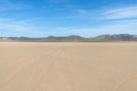 a desert with the desert ground covered in sand and a lone person walking across it