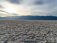 a sunset shines on a sandy desert landscape with mountains and clouds in the background