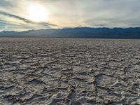 a sunset shines on a sandy desert landscape with mountains and clouds in the background