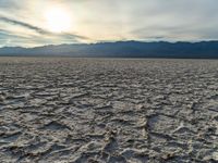 a sunset shines on a sandy desert landscape with mountains and clouds in the background