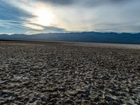 a desert area with dirt and a few clouds in the air over the mountains at sunset