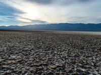 a desert area with dirt and a few clouds in the air over the mountains at sunset