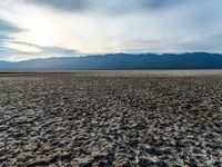 a desert area with dirt and a few clouds in the air over the mountains at sunset