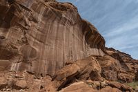 a dirt covered rocky desert with sparse vegetation and rocks and cliffs in the background, with a blue sky in the sky