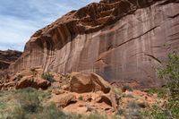 a dirt covered rocky desert with sparse vegetation and rocks and cliffs in the background, with a blue sky in the sky