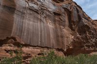 a dirt covered rocky desert with sparse vegetation and rocks and cliffs in the background, with a blue sky in the sky