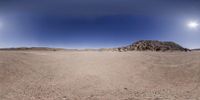 a sky with a few clouds and the sun shining over a desert area with rocky terrain