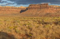 an empty field with rocky terrain near a desert area of brown grass, yellow weeds and brown sky