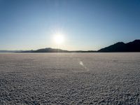 there is snow on the ground on a clear day in the desert, with the sun rising in the distance