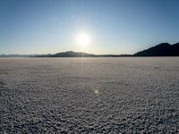 there is snow on the ground on a clear day in the desert, with the sun rising in the distance