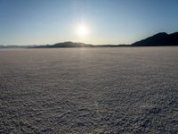 there is snow on the ground on a clear day in the desert, with the sun rising in the distance