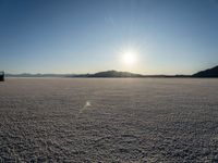 there is snow on the ground on a clear day in the desert, with the sun rising in the distance