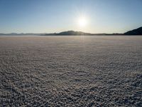 there is snow on the ground on a clear day in the desert, with the sun rising in the distance