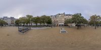 an image of a deserted beach in a city with buildings and trees around it and several benches on the ground