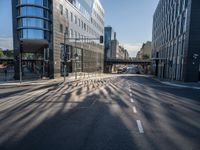 sunlight shines brightly on a deserted city street with buildings and pedestrians on the road