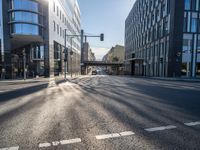 sunlight shines brightly on a deserted city street with buildings and pedestrians on the road