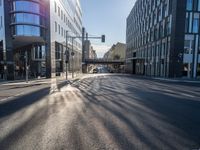 sunlight shines brightly on a deserted city street with buildings and pedestrians on the road