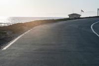 an empty road near a beach and waves as well as cars on the sand and houses on the beach