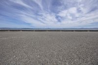 a deserted gravel lot with mountains behind it and blue skies in the sky at the far end