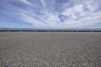 a deserted gravel lot with mountains behind it and blue skies in the sky at the far end