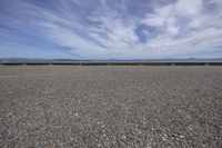 a deserted gravel lot with mountains behind it and blue skies in the sky at the far end