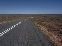 a deserted highway in the middle of a desert landscape in australia, with a lone sign on one side and some grass and scrub land