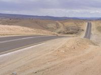 a motorcycle on a deserted highway in the desert with mountains in the background and a cloudy sky