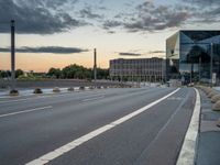 a deserted highway is shown in a city at sunset with a glass building near by