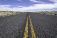 a deserted long road stretching into the distance in a desert landscape with blue skies and fluffy clouds