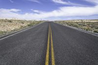 a deserted long road stretching into the distance in a desert landscape with blue skies and fluffy clouds