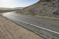 a motorcycle riding down a winding highway between hills and dry grass on a sunny day