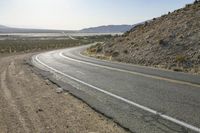 a motorcycle riding down a winding highway between hills and dry grass on a sunny day
