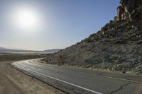 a motorcycle riding down a winding highway between hills and dry grass on a sunny day