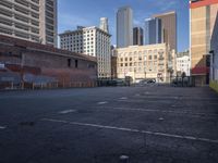 a deserted parking lot is shown with graffiti on the wall and tall buildings in the background