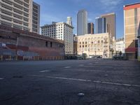 a deserted parking lot is shown with graffiti on the wall and tall buildings in the background