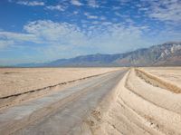 a deserted road in the desert with mountains in the background and water flowing through it