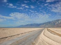 a deserted road in the desert with mountains in the background and water flowing through it